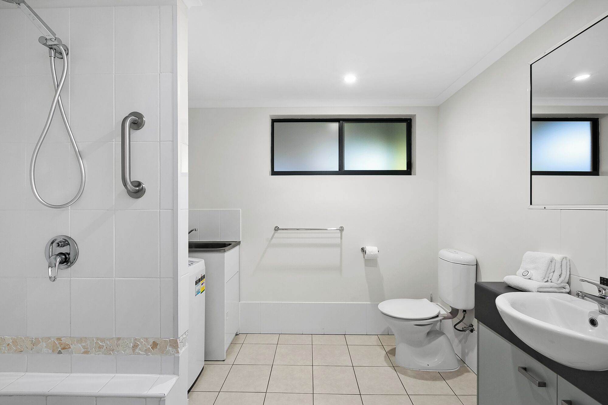 Ein modernes Badezimmer mit Dusche, Toilette, Waschbecken und einem Fenster.