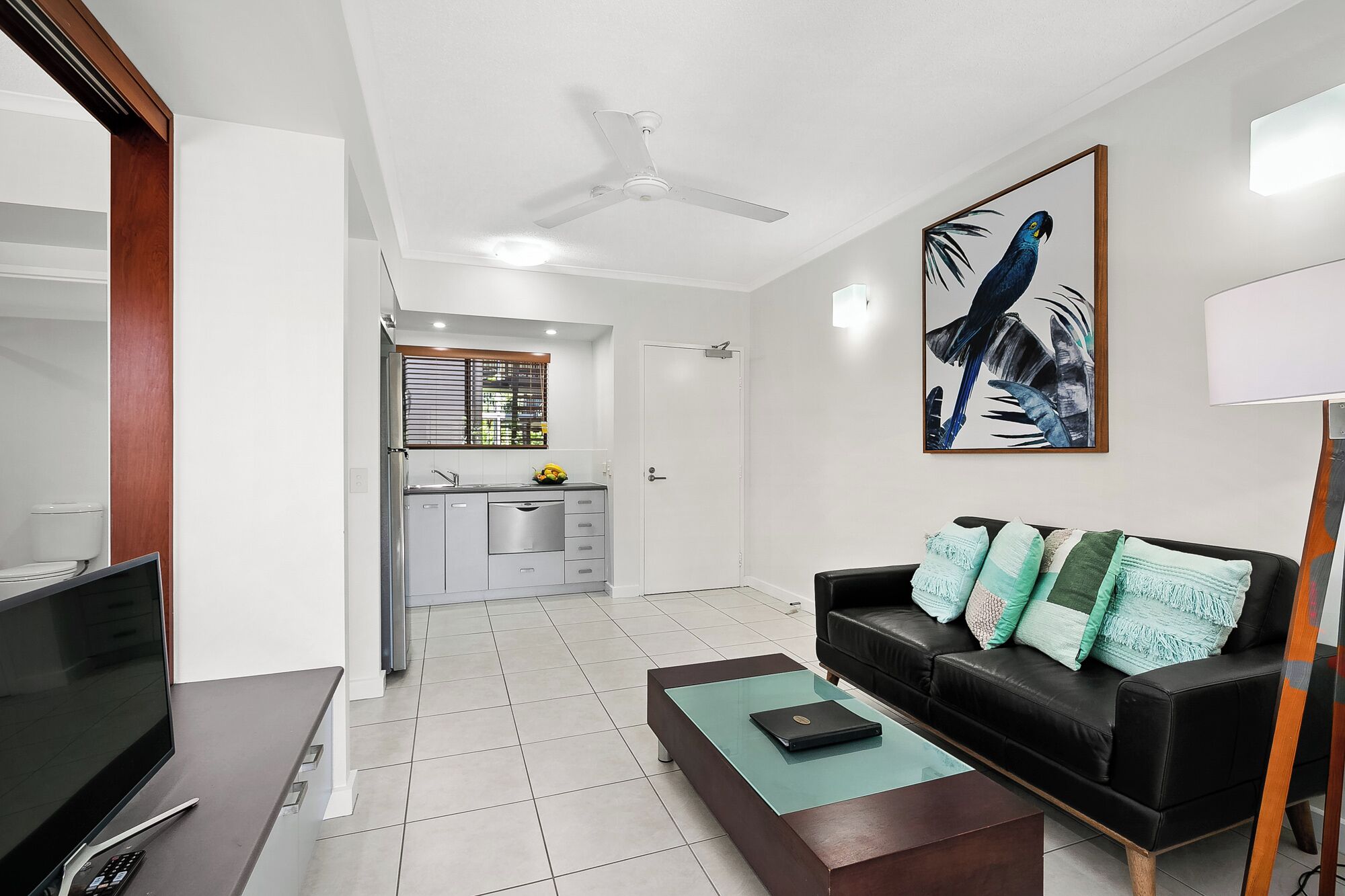 A modern living room with a black leather sofa, a glass coffee table, and a TV stand.