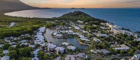 Vista aérea de un complejo turístico costero con un puerto deportivo, abundante vegetación y una combinación de edificios residenciales y comerciales.