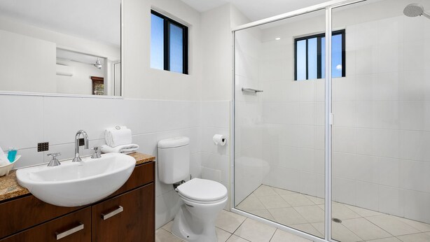 A modern bathroom with a glass shower enclosure, a white sink, and a toilet. - Blue Lagoon Resort (Trinity Beach)
