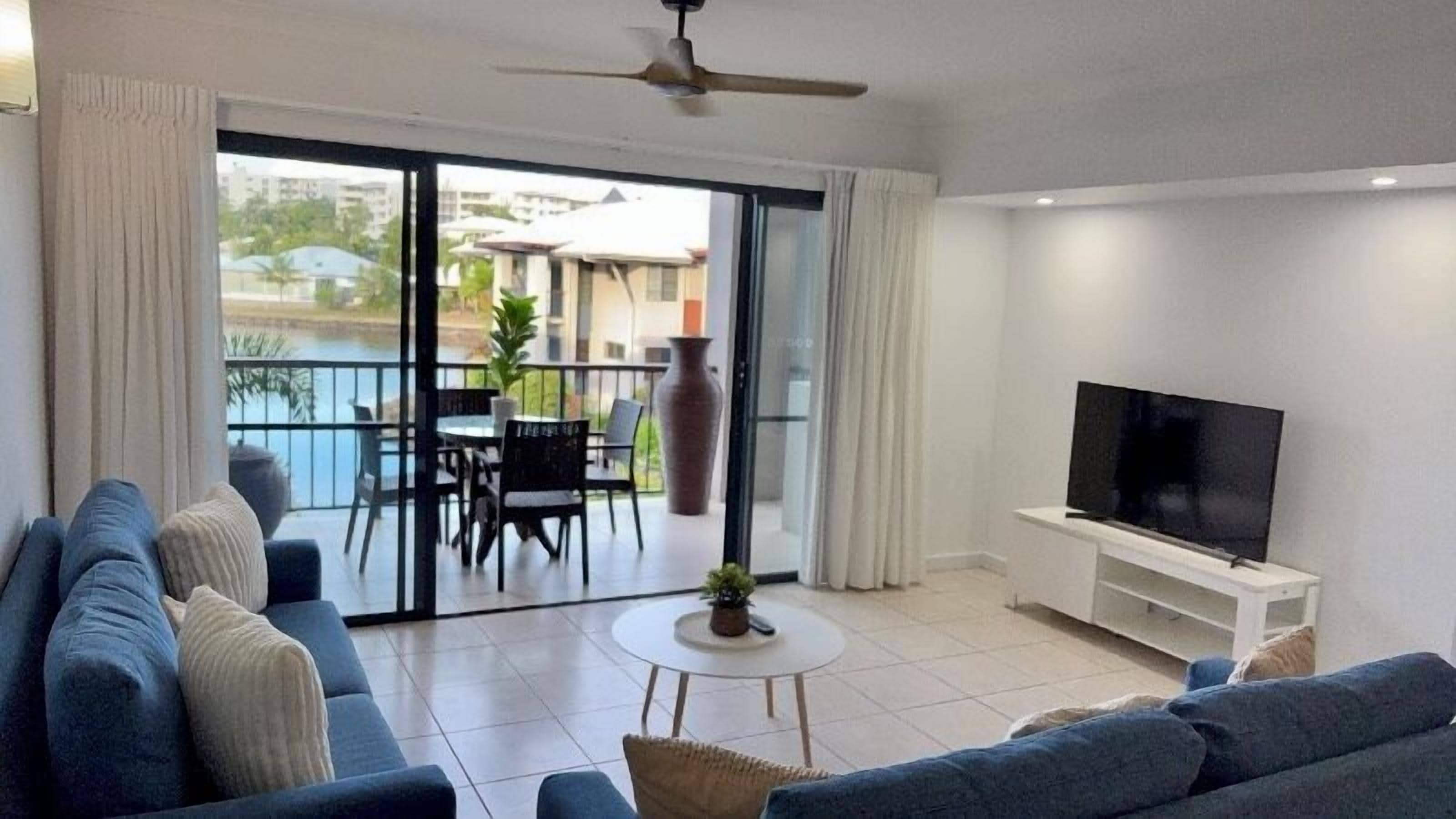 A living room with a sofa, a TV, and a balcony with a table and chairs.