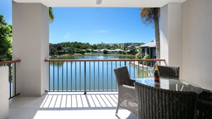 A balcony with a glass table and wicker chairs, overlooking a lake and buildings. - Blue Lagoon Resort (Trinity Beach)