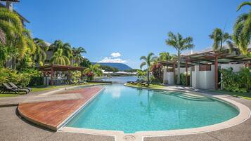 A resort pool with a wooden deck, lounge chairs, and palm trees.