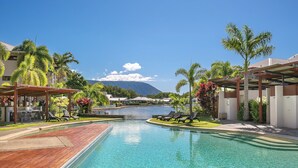 A clear blue pool with wooden deck, lounge chairs, and palm trees. - Blue Lagoon Resort (Trinity Beach)