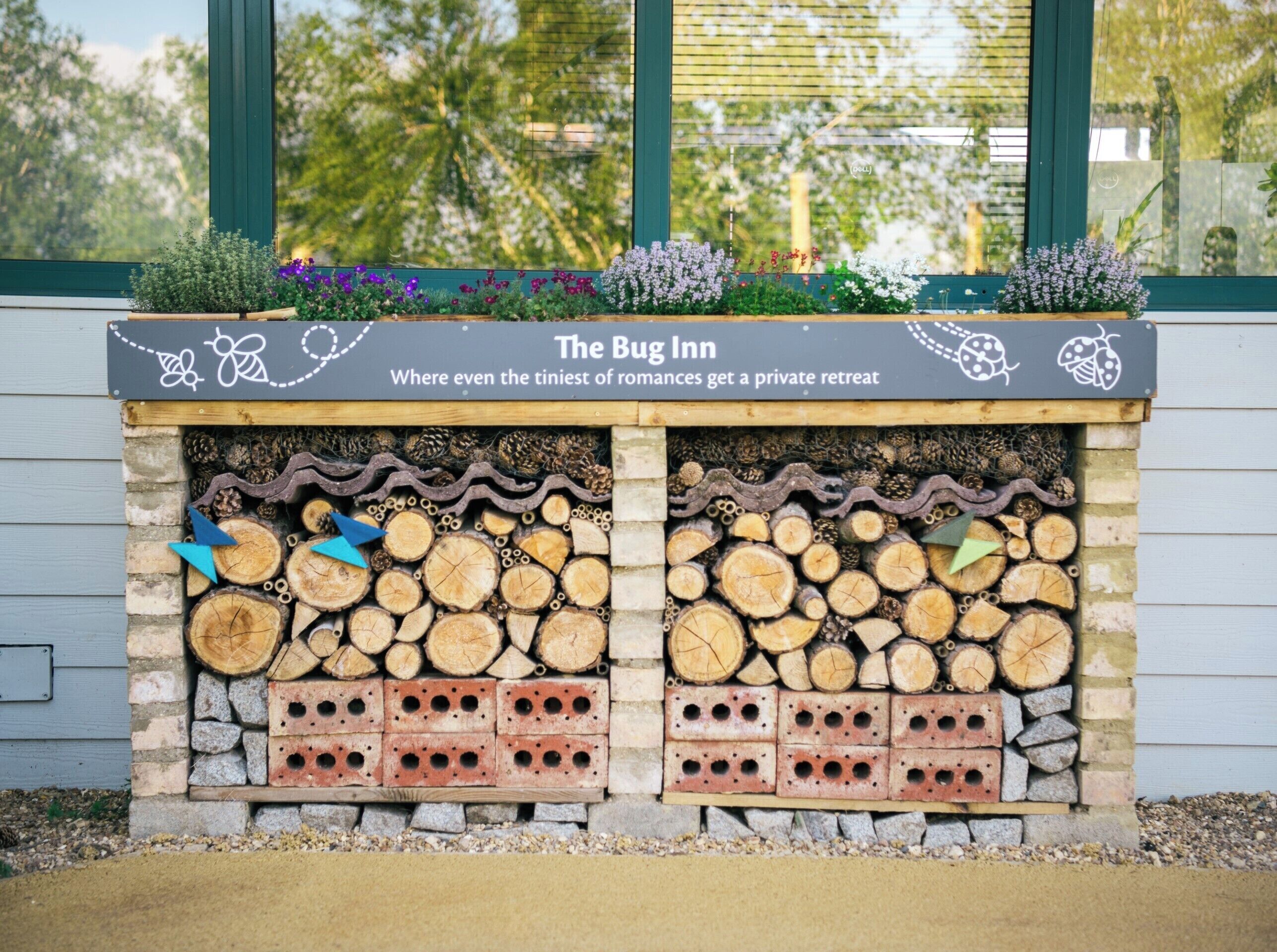 Eine Wand aus Baumstämmen und Ziegelsteinen, mit der Aufschrift "The Bug Inn" und einem Schild, das verkündet: "Auch die kleinsten Romanzen finden hier einen Rückzugsort."