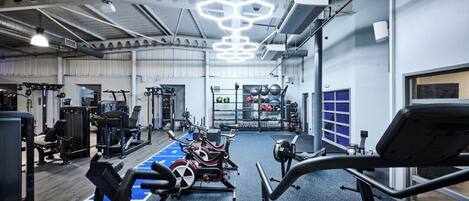 A gym with exercise equipment, a blue exercise area, and a ceiling with hexagonal light fixtures.