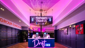 A Driftn Inn reception area with a 'Bedroom Check In' sign, a 'Group Check In' sign, and a wall-mounted TV screen. - Drift Inn at Wyboston Lakes (Bedford)