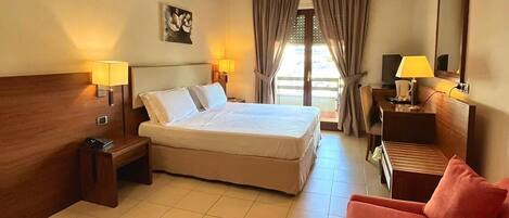 A hotel room with a bed, bedside tables, a desk, a chair, and a red sofa.
