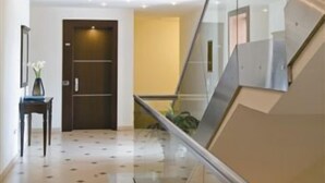 Un interior moderno con una escalera de cristal, piso de baldosas y una puerta con marco oscuro.