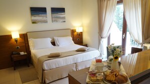 Habitación de hotel con cama, lámparas de noche, mesita auxiliar, bandeja con alimentos para el desayuno y ventana con cortinas.