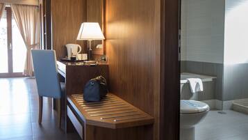 Una habitación de hotel moderna con un escritorio de madera, una silla, una lámpara y un baño con inodoro y lavamanos.