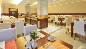 Un comedor de hotel con varias mesas y sillas, una barra de buffet y un mostrador de recepción.