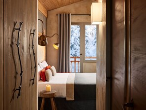 Un dormitorio acogedor con cama, mesita de noche, lámpara y ventana con vista a árboles nevados.