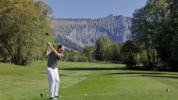 Golfers can enjoy a challenging game amidst lush greenery and a scenic mountainous backdrop.
