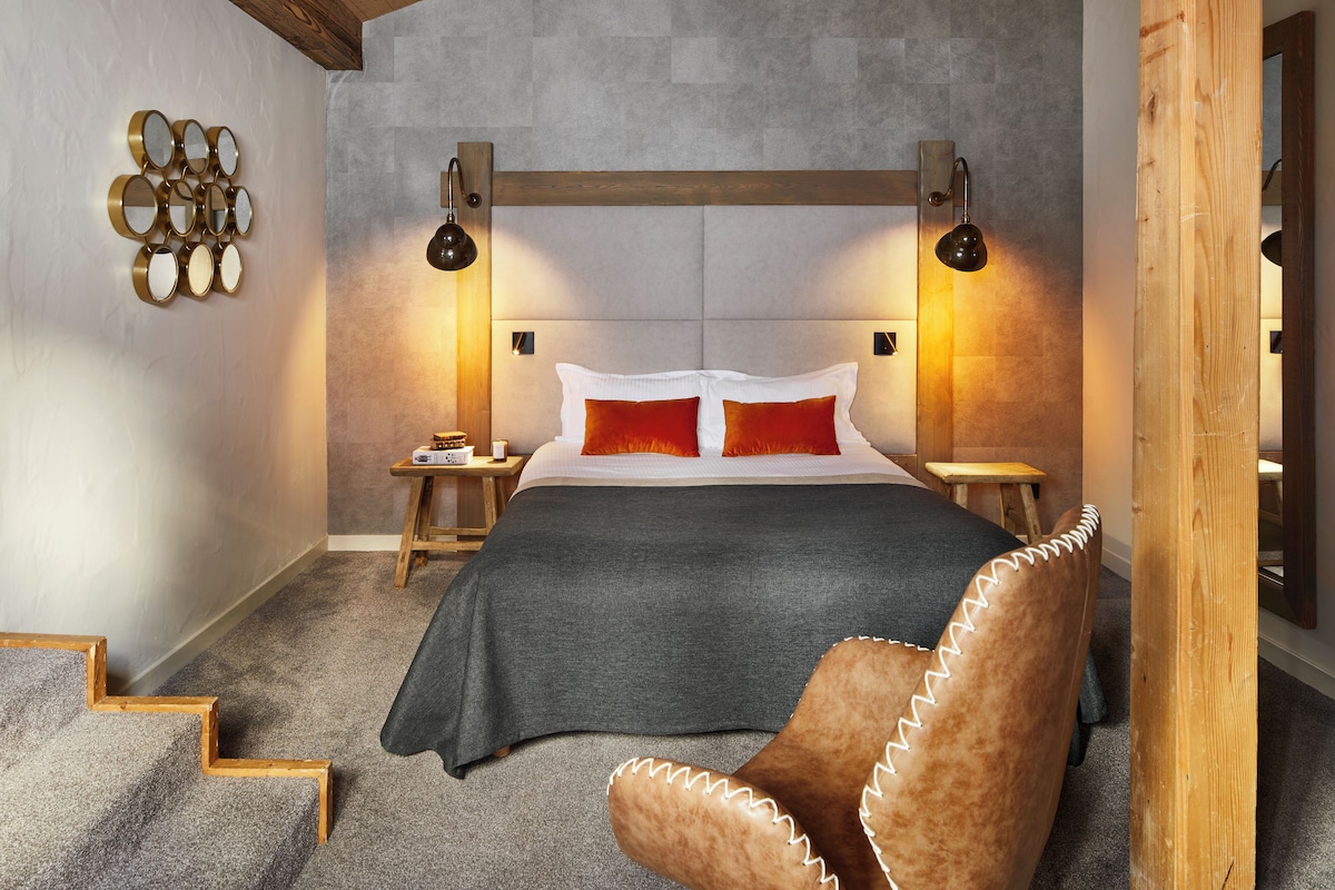 A bedroom with a bed, two bedside tables, a wall-mounted mirror, and a wooden chair.