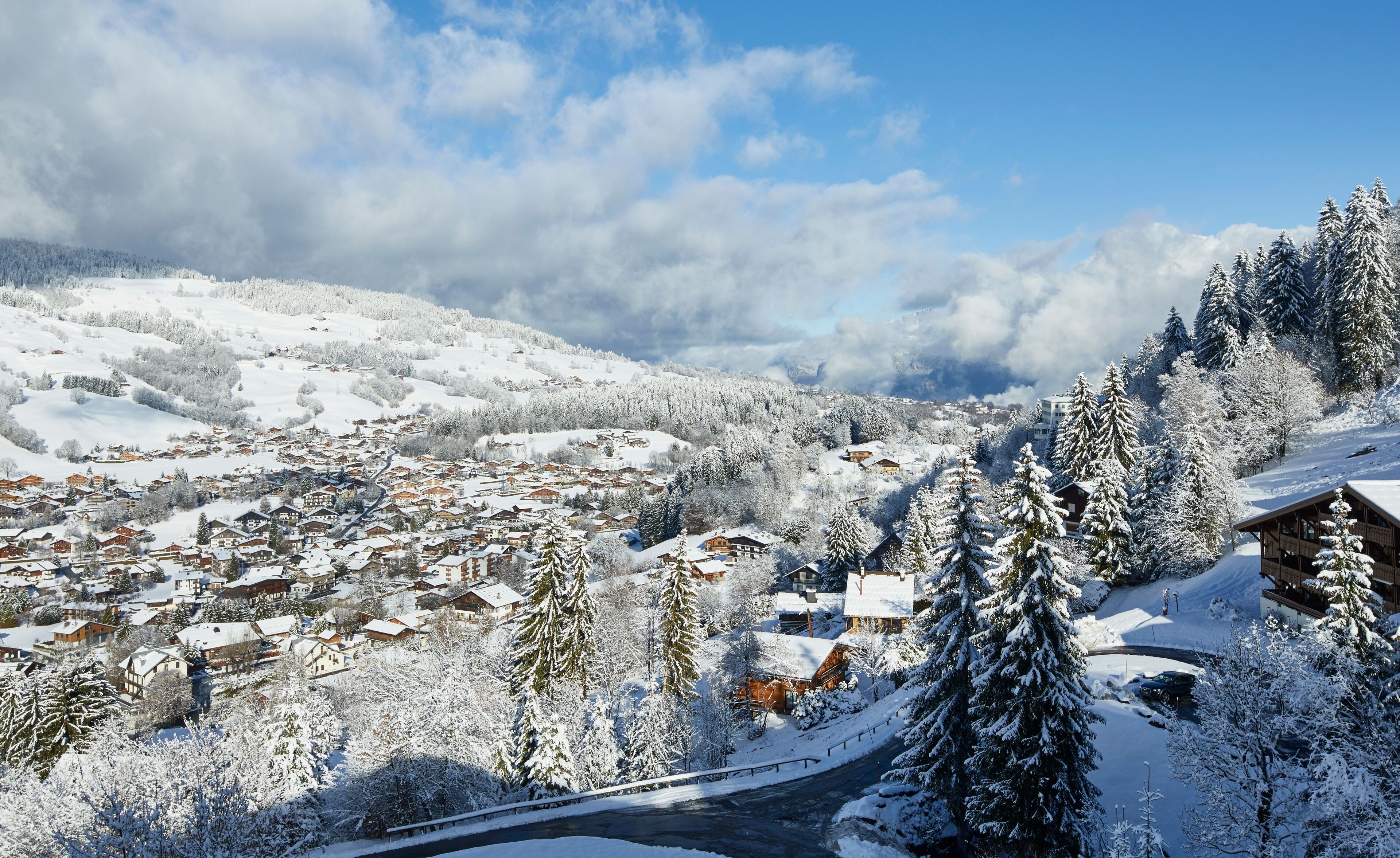 A snow-covered village with traditional wooden houses, a winding road, and a mountain backdrop.