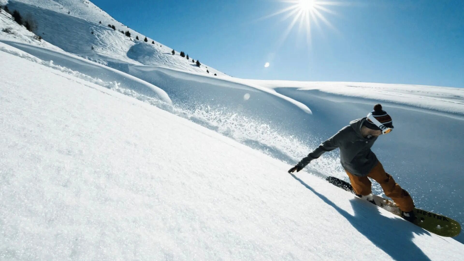 A snowboarder on a snowy slope with a clear sky and sun.