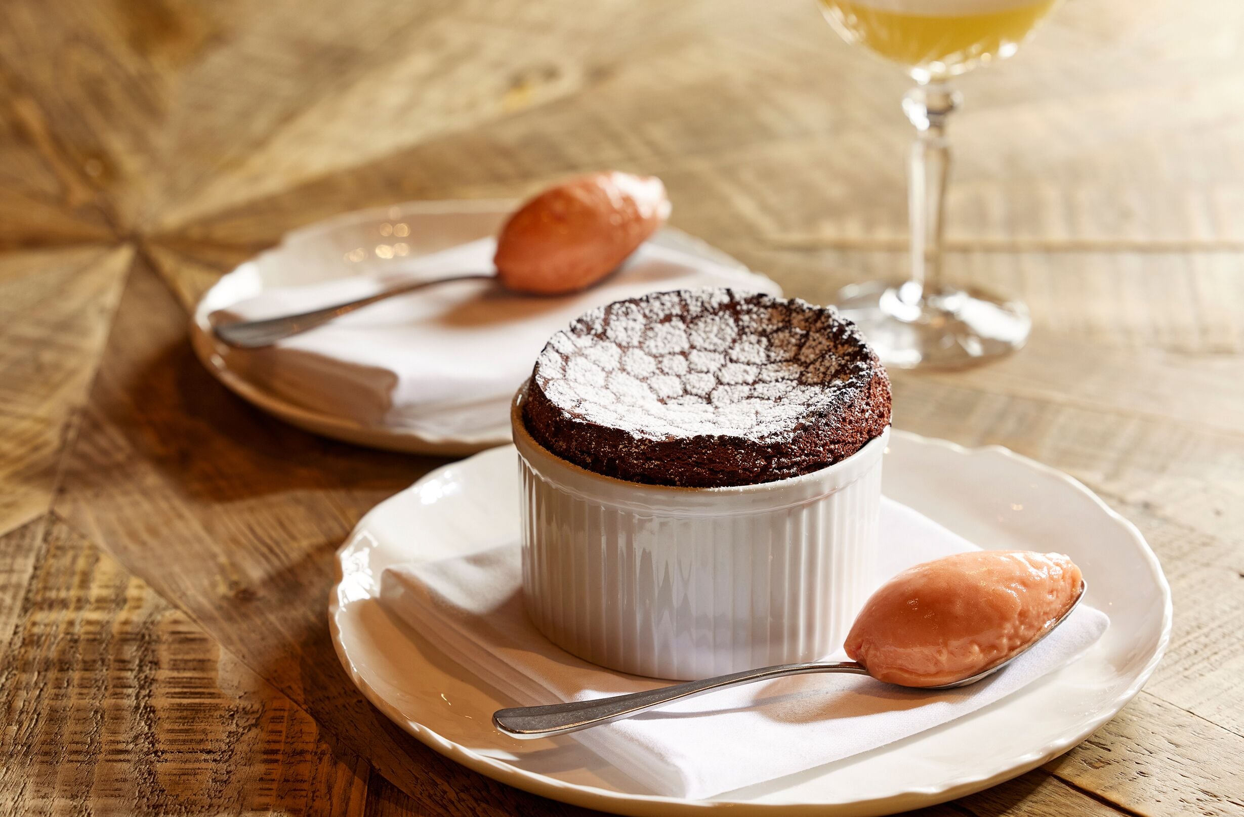 Un dessert su un piatto bianco, con un cucchiaio e, sullo sfondo, un bicchiere di bevanda gialla.