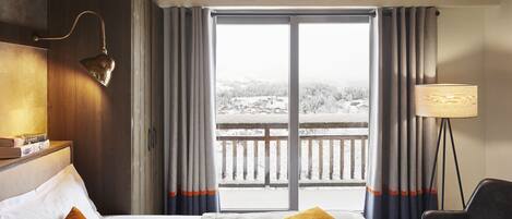 Una habitación de hotel con una cama, una silla, una lámpara y vistas a un paisaje nevado a través del ventanal.