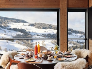 A breakfast table set with various dishes and drinks, overlooking a snowy landscape through large windows. - Hôtel l'Arboisie (Megeve)