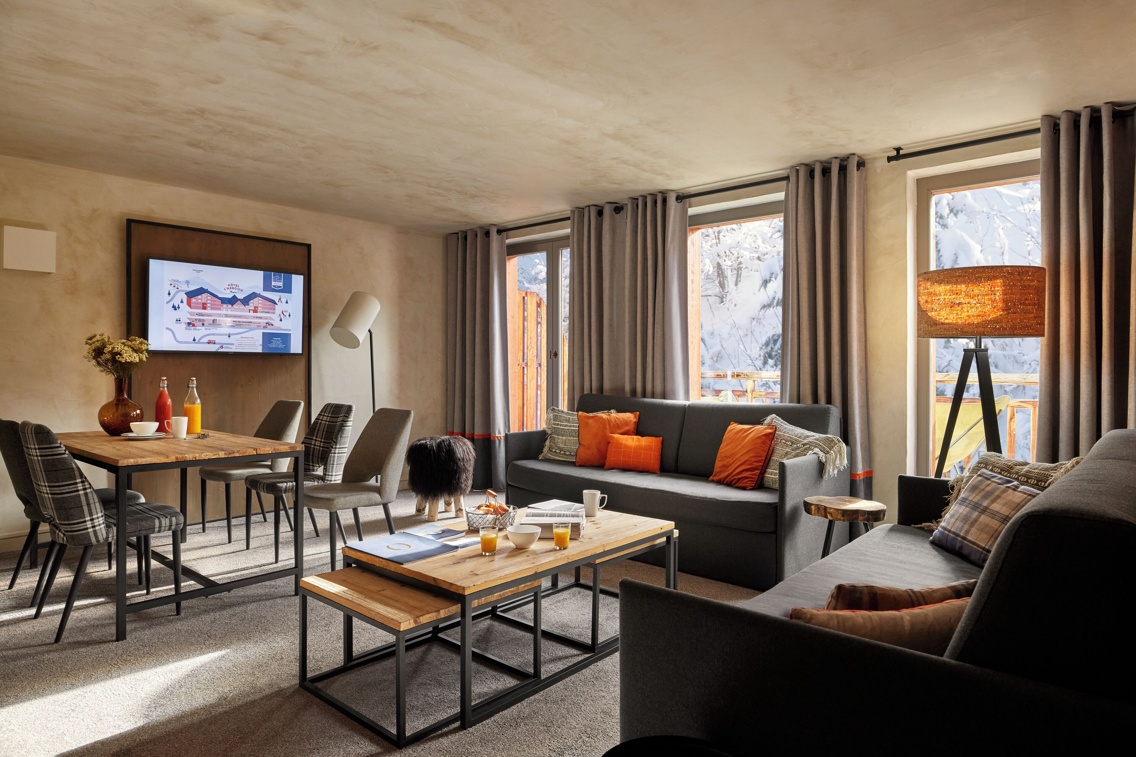 Un salon moderne avec un canapé, une table basse et un coin repas. Un téléviseur est fixé au mur et il y a une fenêtre avec des rideaux.