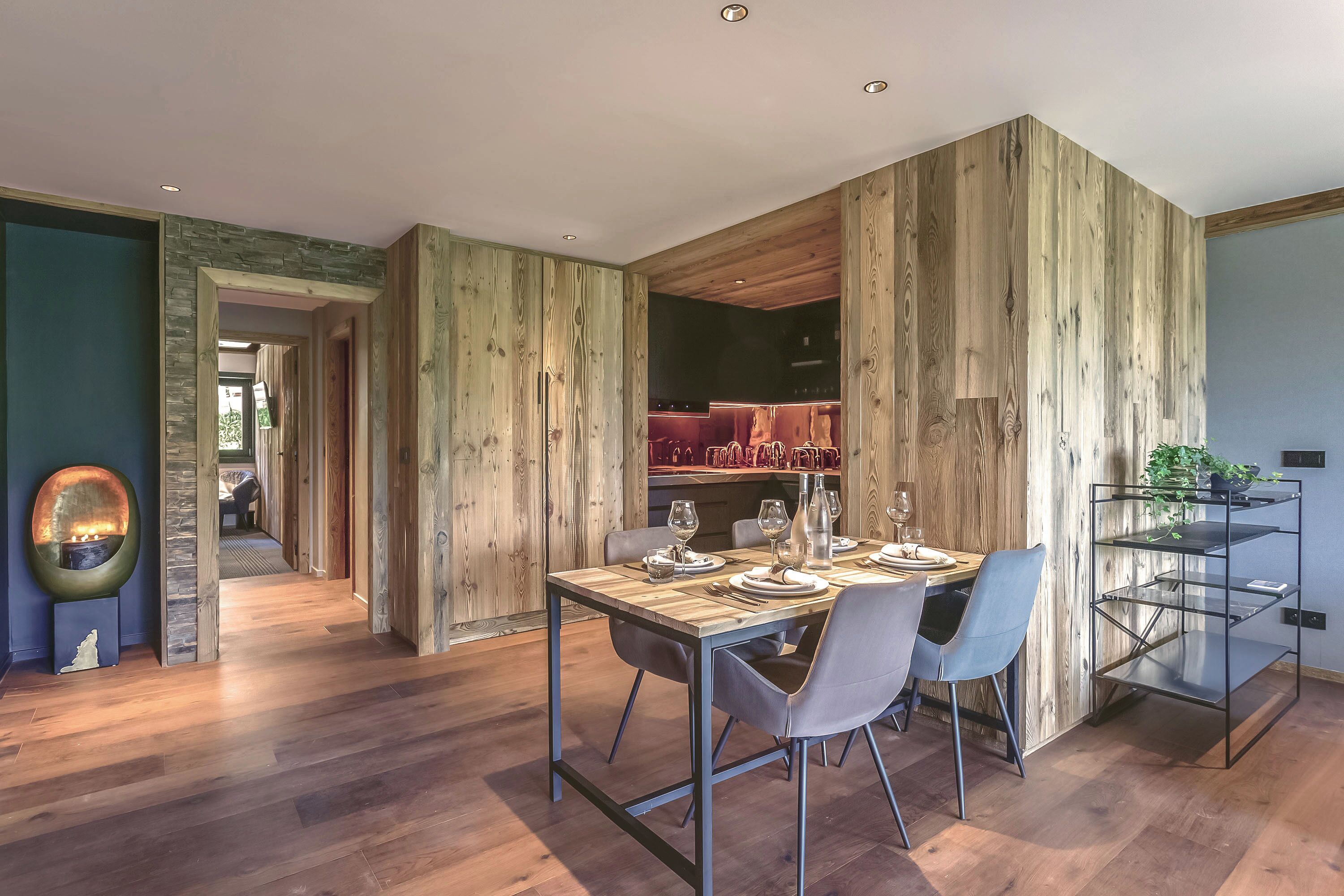 A modern dining area with a wooden accent wall, a dining table set for two, and a metal shelving unit with plants.