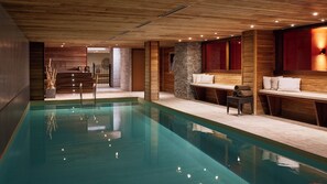 A modern indoor swimming pool with wooden walls and a stone accent wall. - Hôtel l'Arboisie (Megeve)