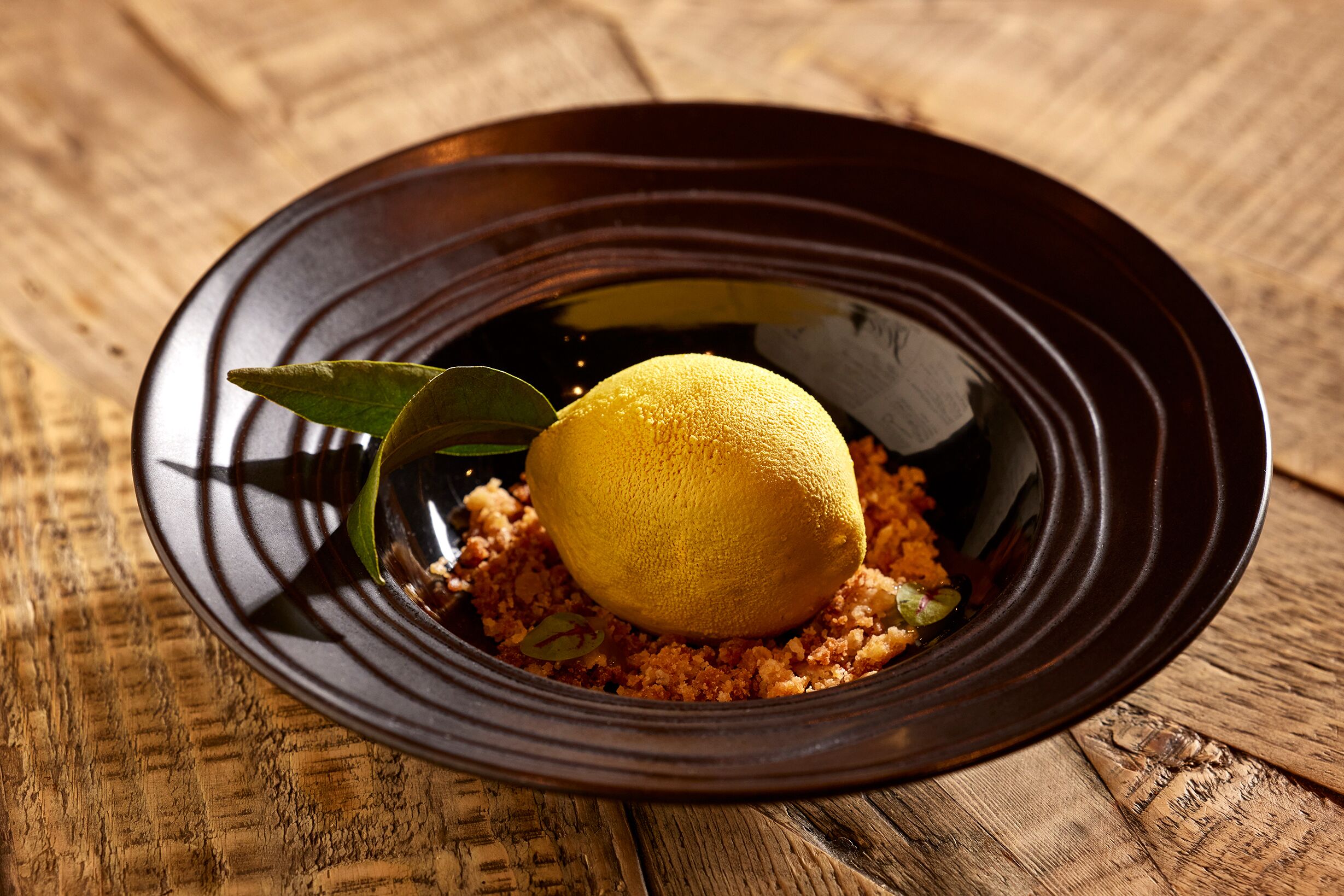 Ein Dessert mit Zitrone auf einem dunklen Teller auf einem Holztisch.