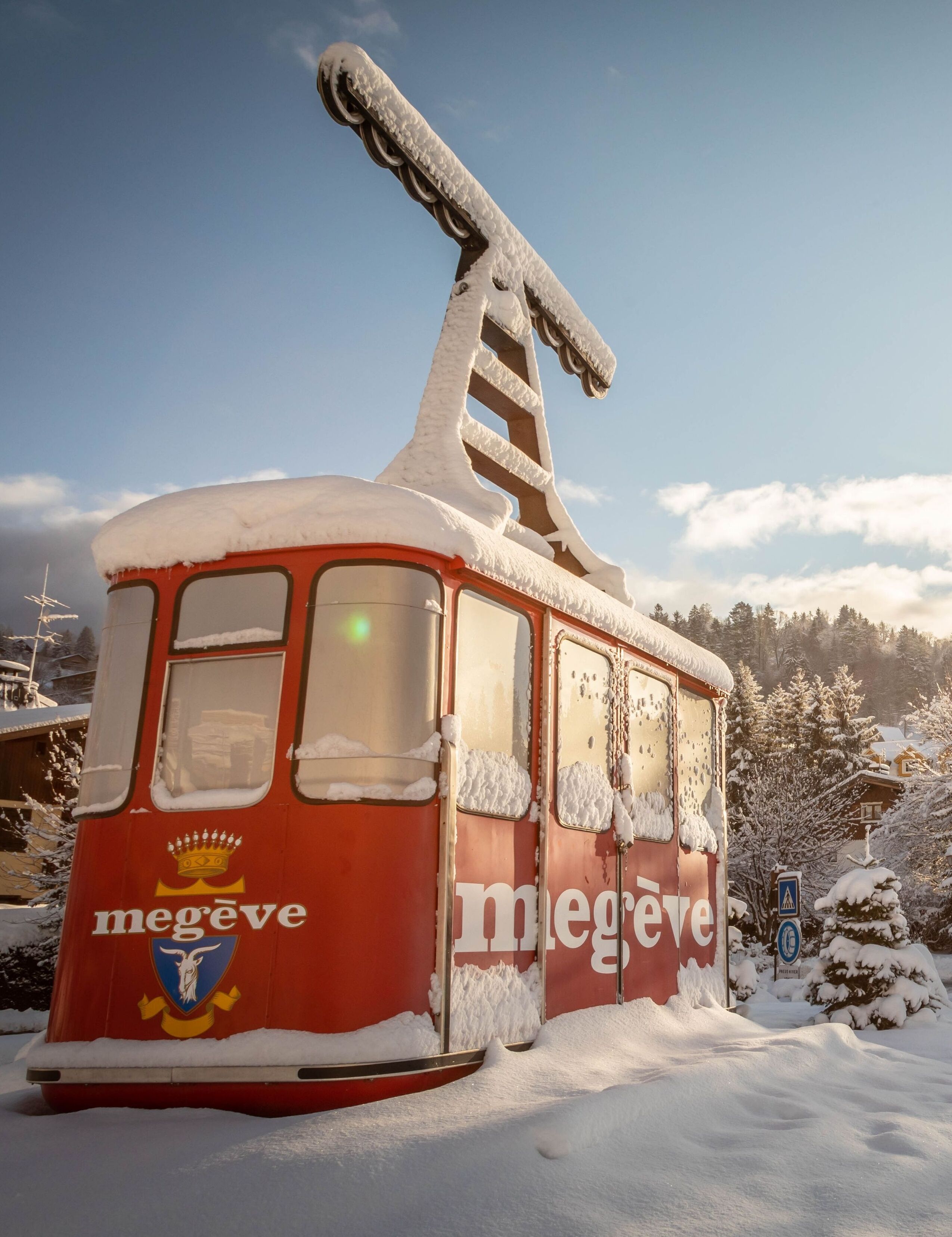Um funicular vermelho com a palavra "Megève" na lateral, coberto de neve, estacionado em uma área nevada.