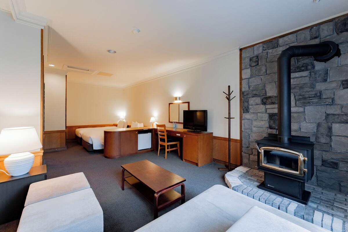 A hotel room with a bed, desk, chair, television, fireplace, and a lamp.