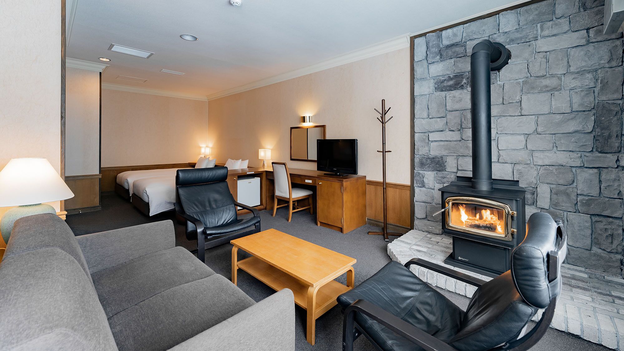 A hotel room with a fireplace, sofa, armchair, desk, and television.
