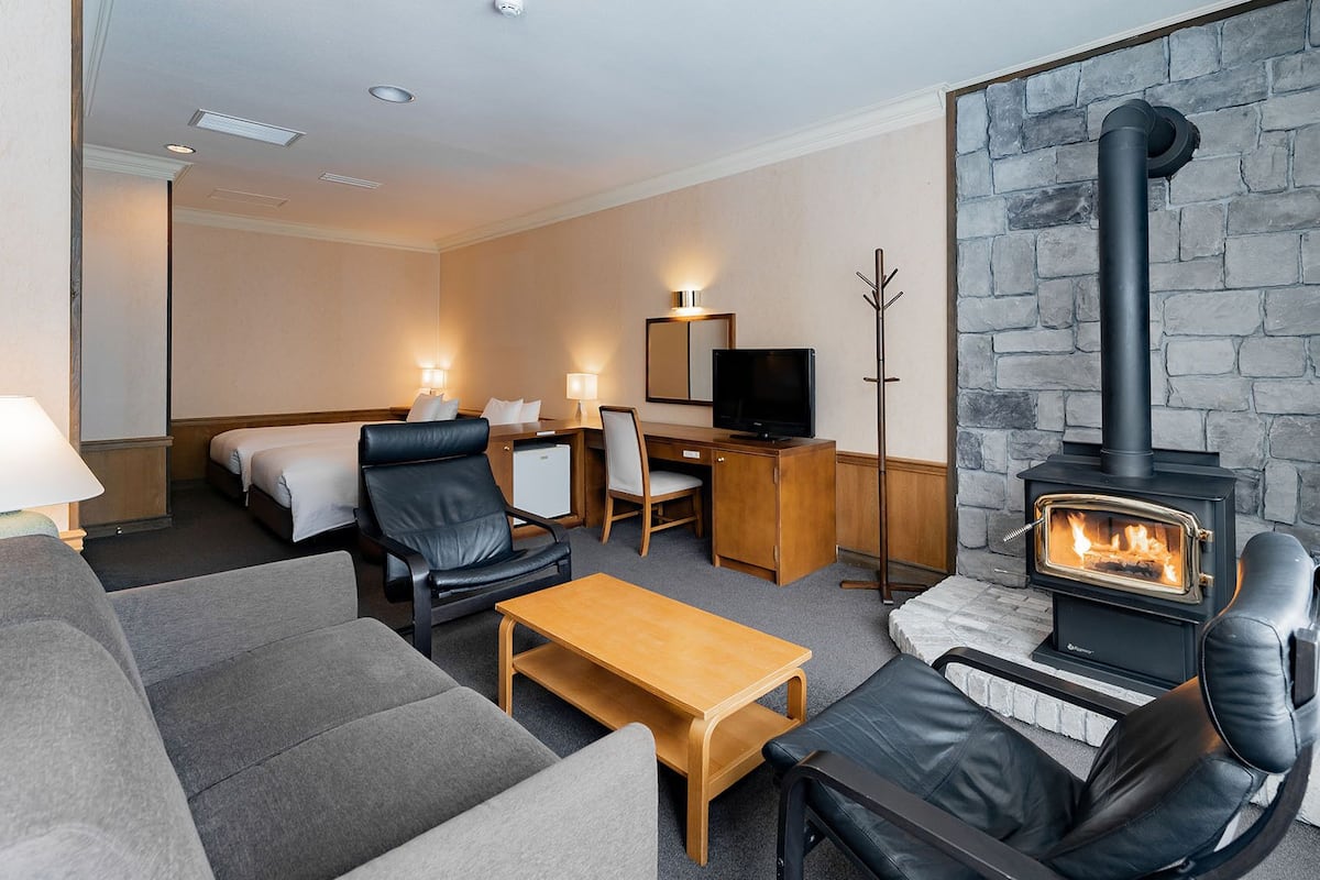 A hotel room with a fireplace, sofa, armchair, desk, and television.