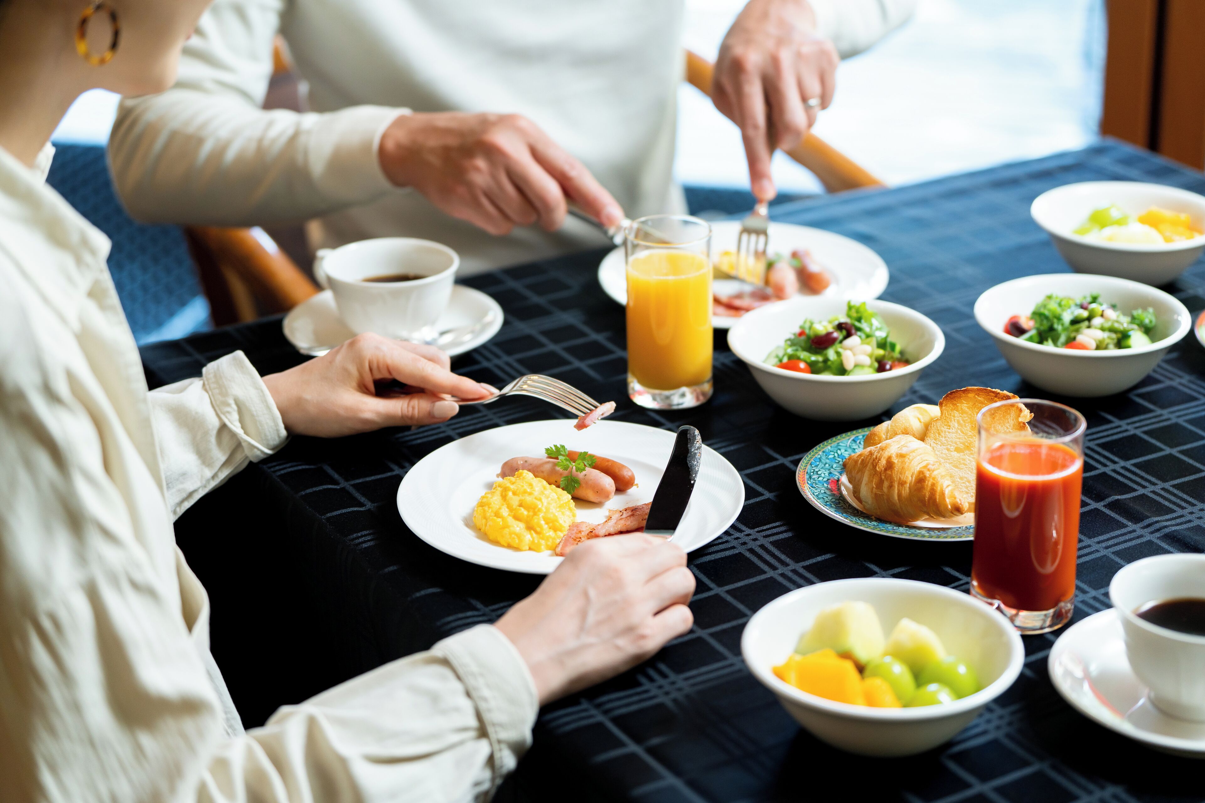 A breakfast setting with plates of food, a glass of orange juice, and a croissant.