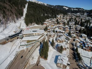 Un pueblo cubierto de nieve con edificios de estilo chalete tradicional, un telesilla y una carretera con vehículos.