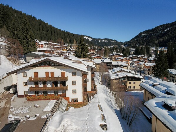 Un pueblo cubierto de nieve con edificios tradicionales de madera, incluyendo un hotel con balcón y un letrero.
