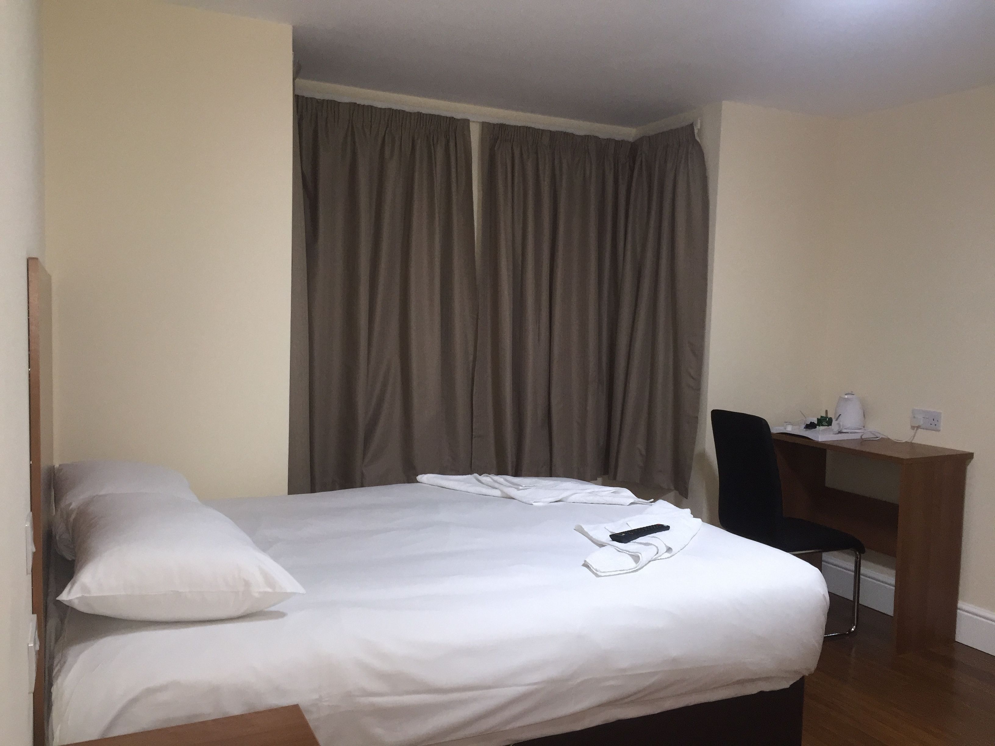 A hotel room with a bed, a desk, a chair, and a curtain.