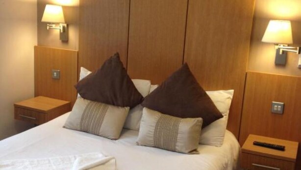Quarto de hotel com uma cama grande, duas mesas de cabeceira e cabeceira de madeira.