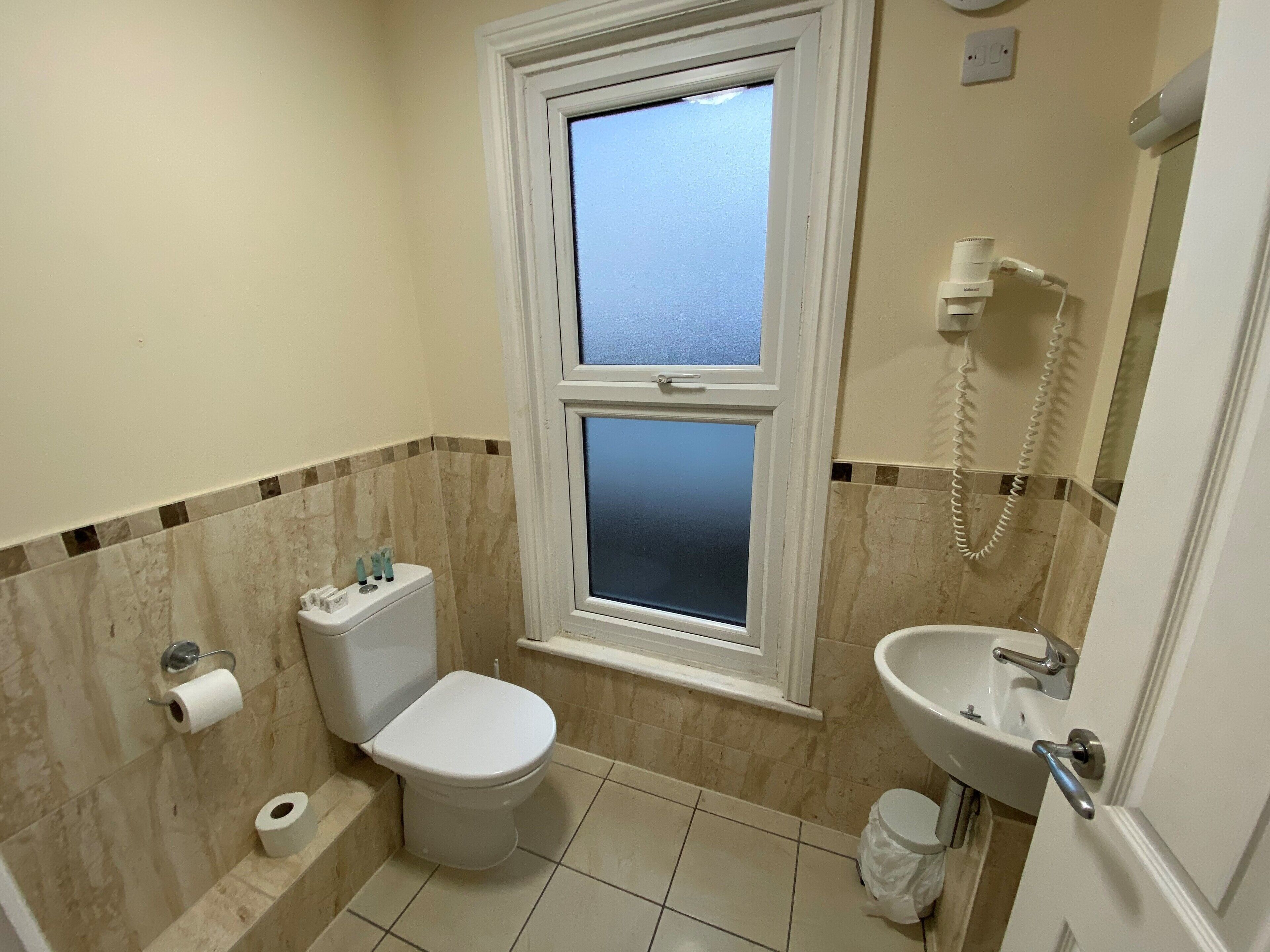 Une petite salle de bain propre, équipée de toilettes, d’un lavabo et d’une fenêtre.