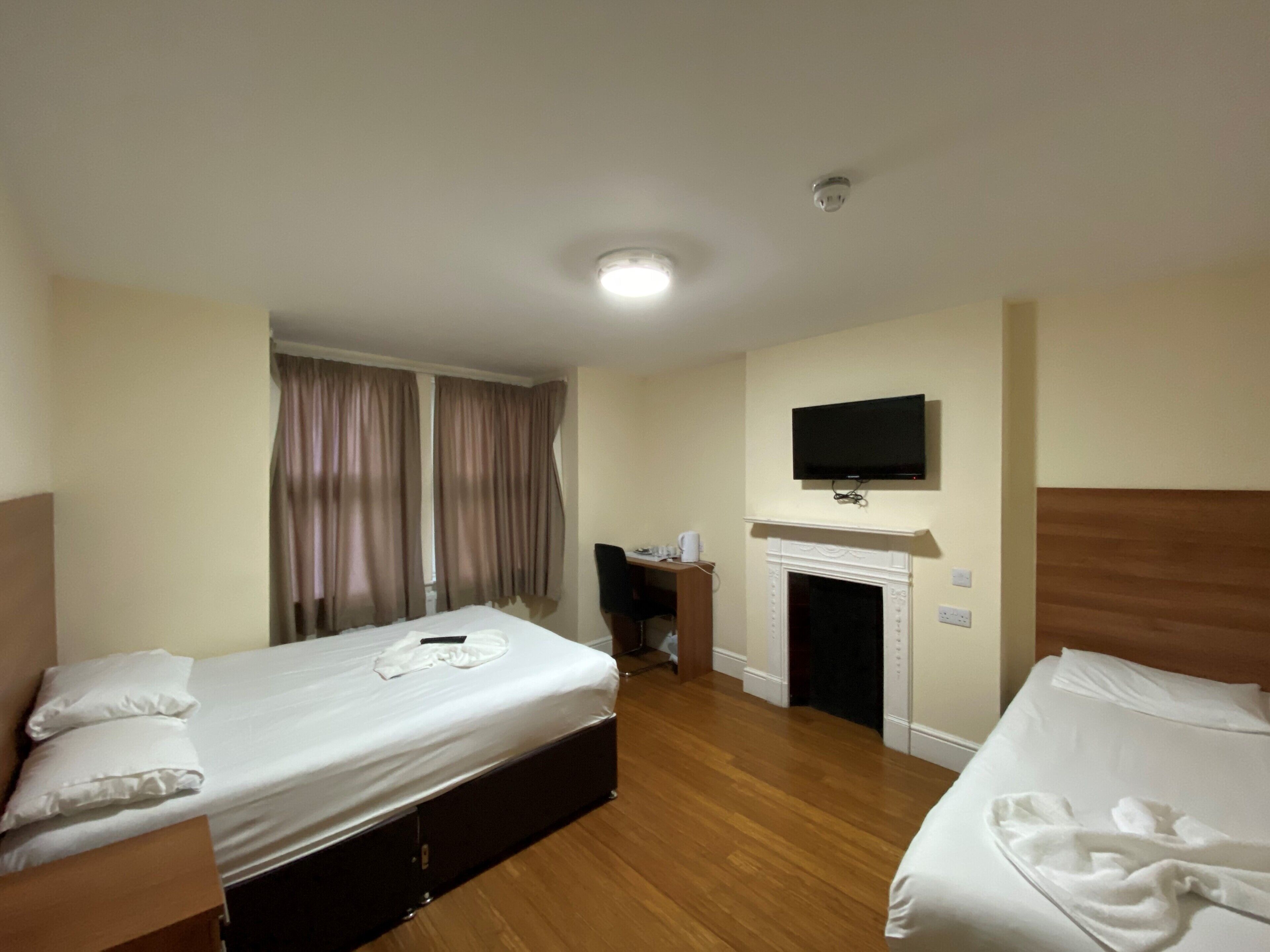 Quarto de hotel com duas camas, uma escrivaninha, uma cadeira, uma televisão e uma lareira.