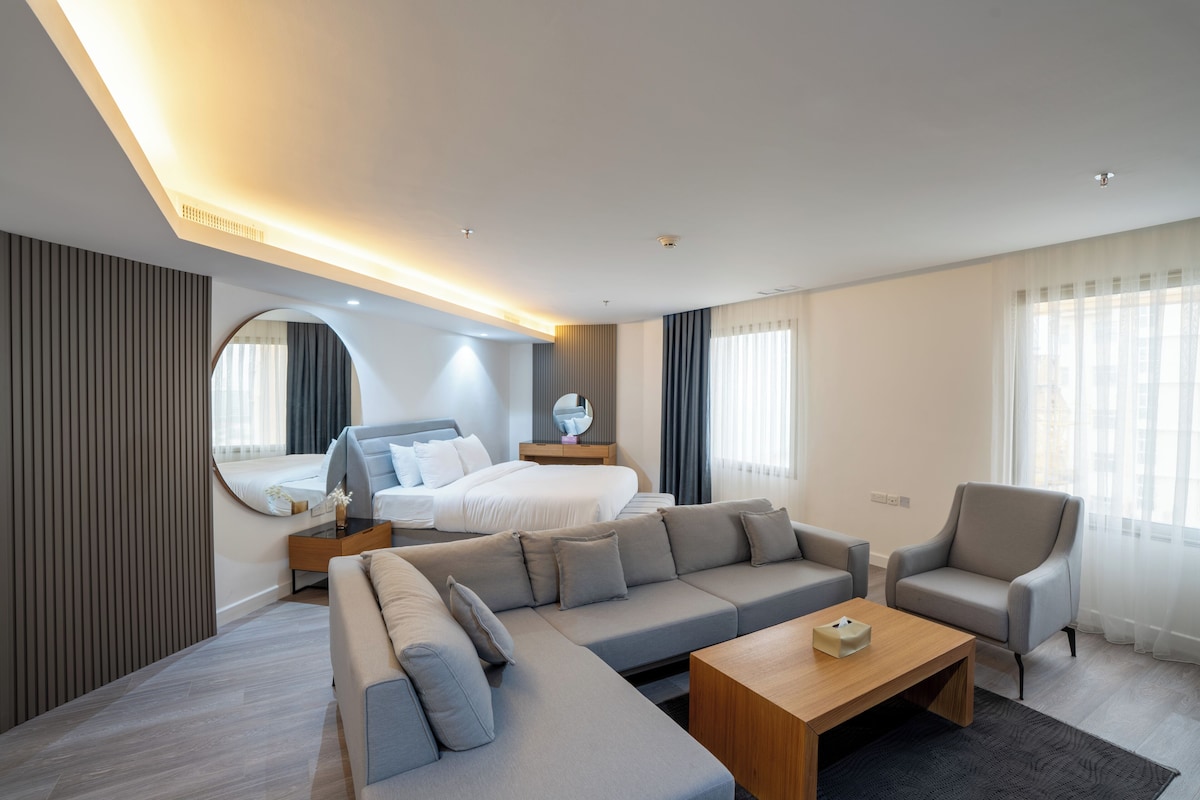 Quarto de hotel moderno com uma cama grande, um sofá, uma cadeira e uma mesinha.