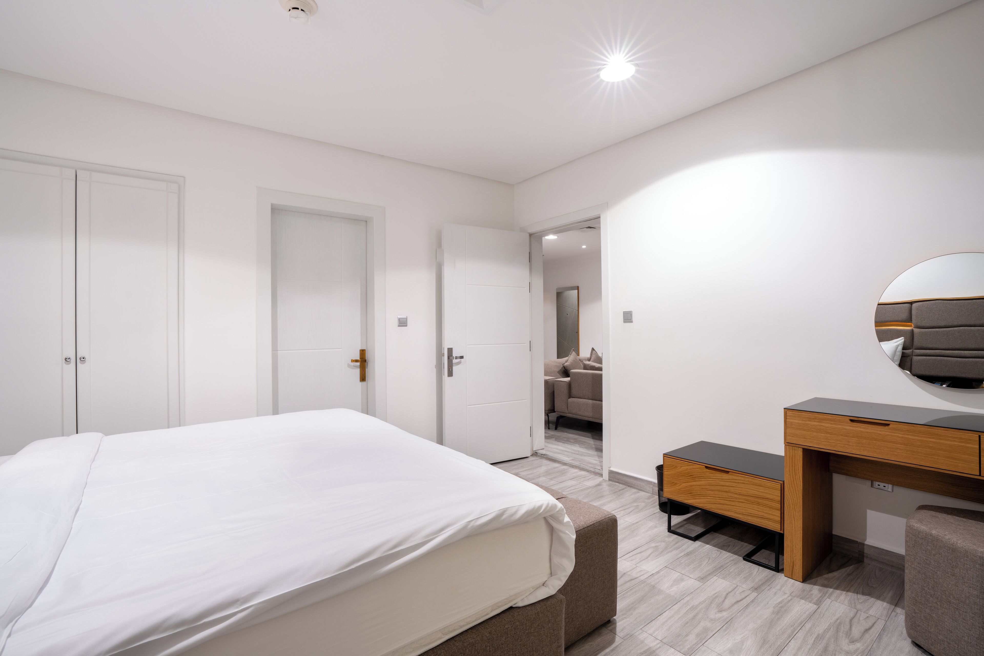 Un dormitorio moderno con una cama grande, un escritorio y una silla. Hay dos puertas y un pasillo que conduce a otra habitación.