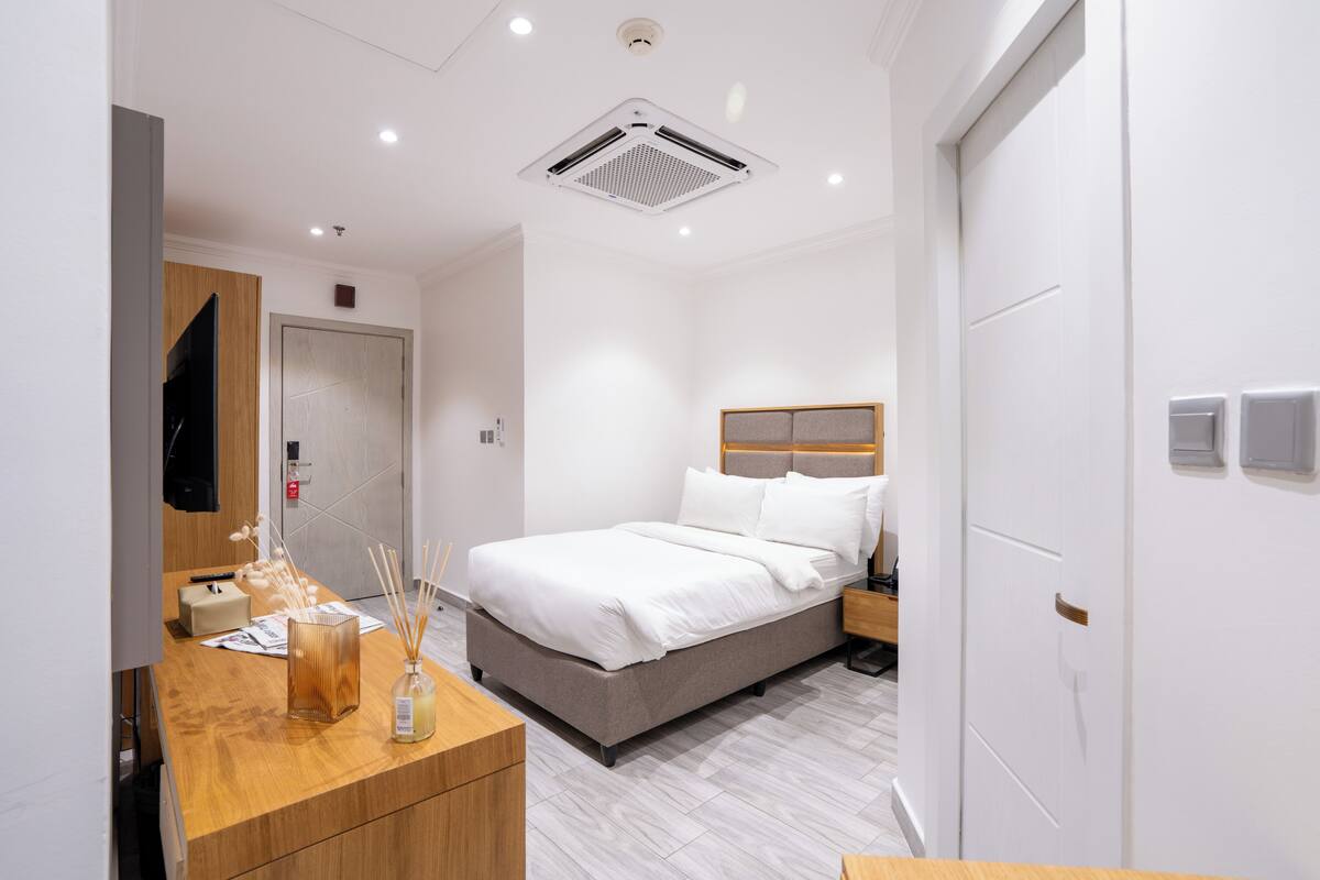 A modern hotel room with a bed, wooden dresser, and a mirror.