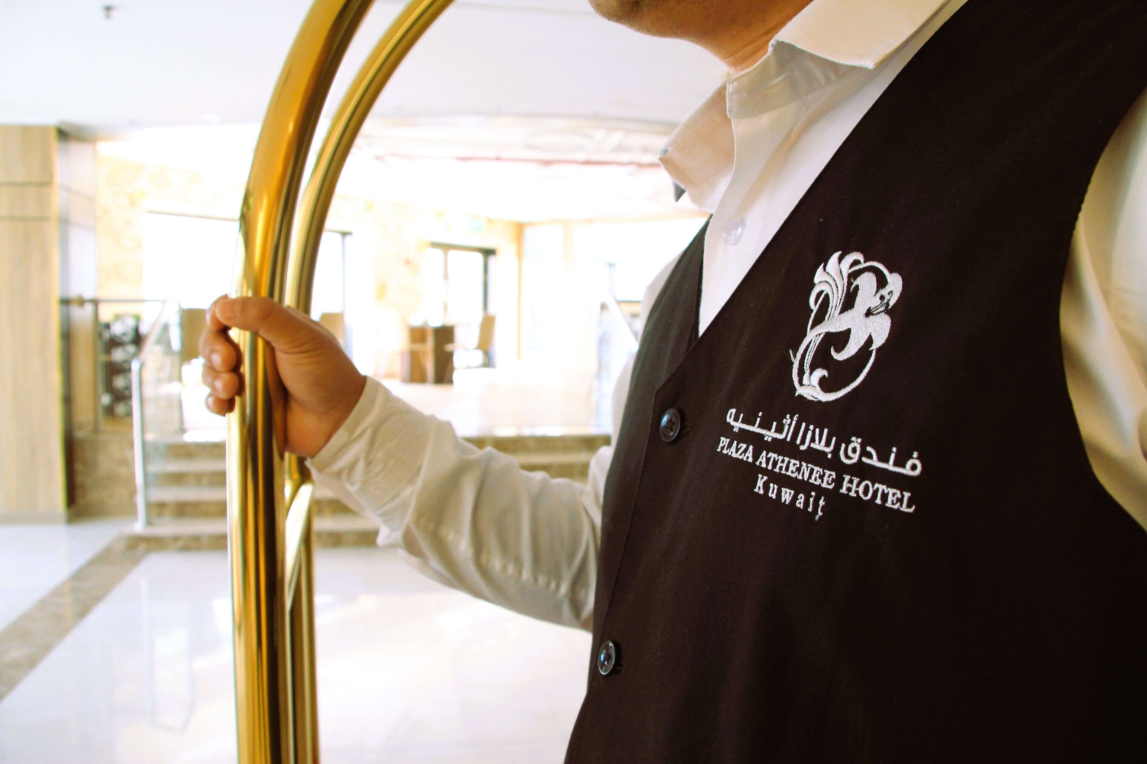 A person in a black vest with a logo and text indicating the Plaza Athenee Hotel in Kuwait.