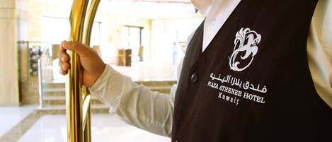 A person in a black vest with a logo and text indicating the Plaza Athenee Hotel in Kuwait.