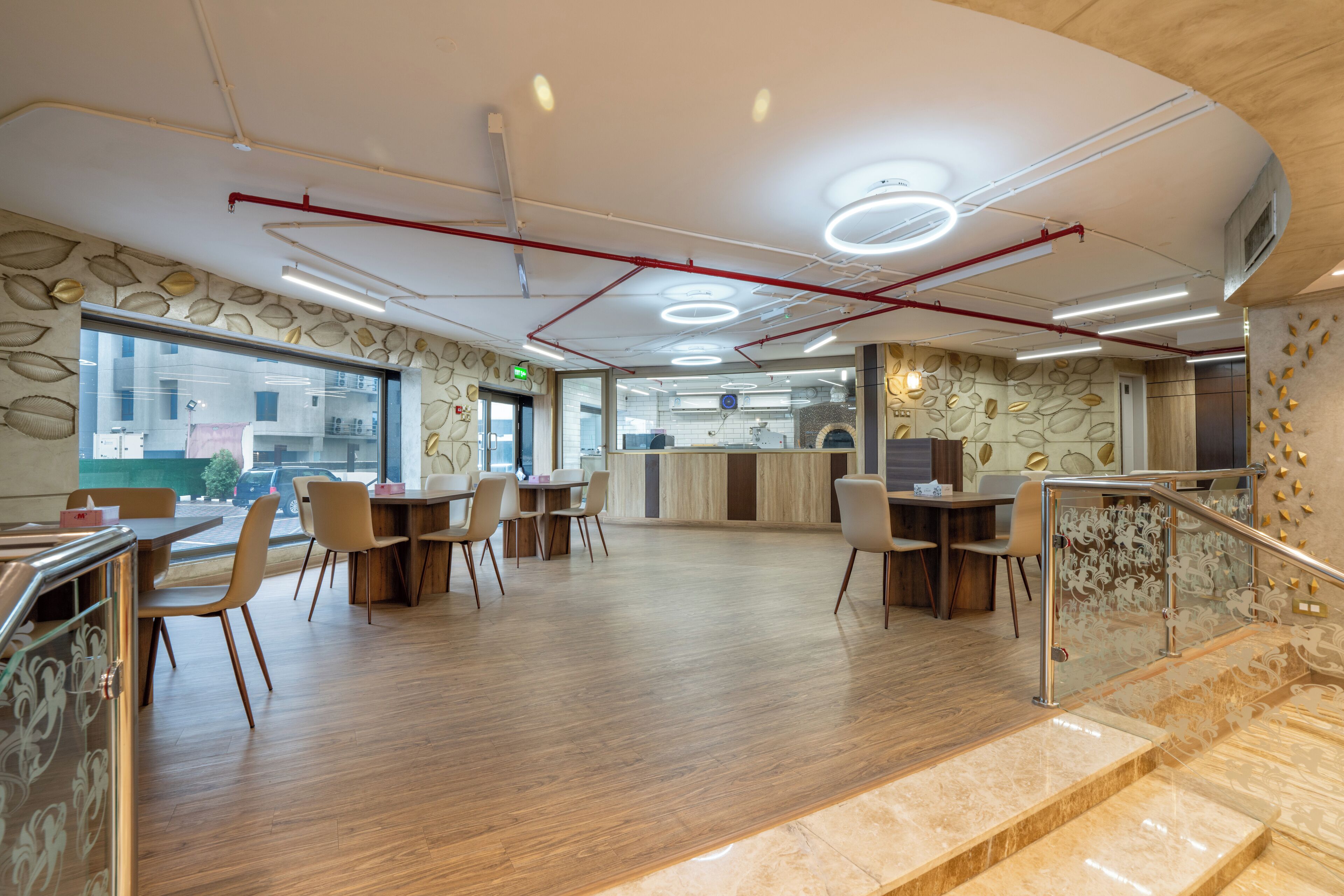 A spacious restaurant with wooden flooring, modern chairs, a counter, and a staircase with glass railings.