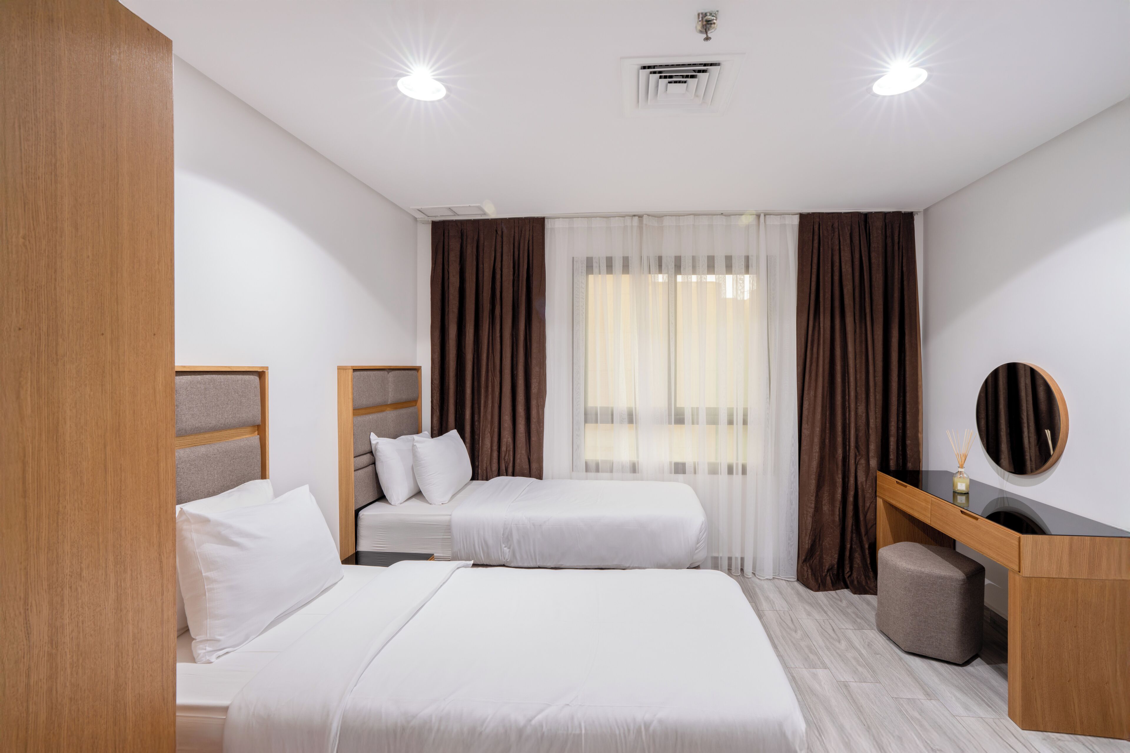 A hotel room with two beds, a desk, a chair, and a large window with curtains.