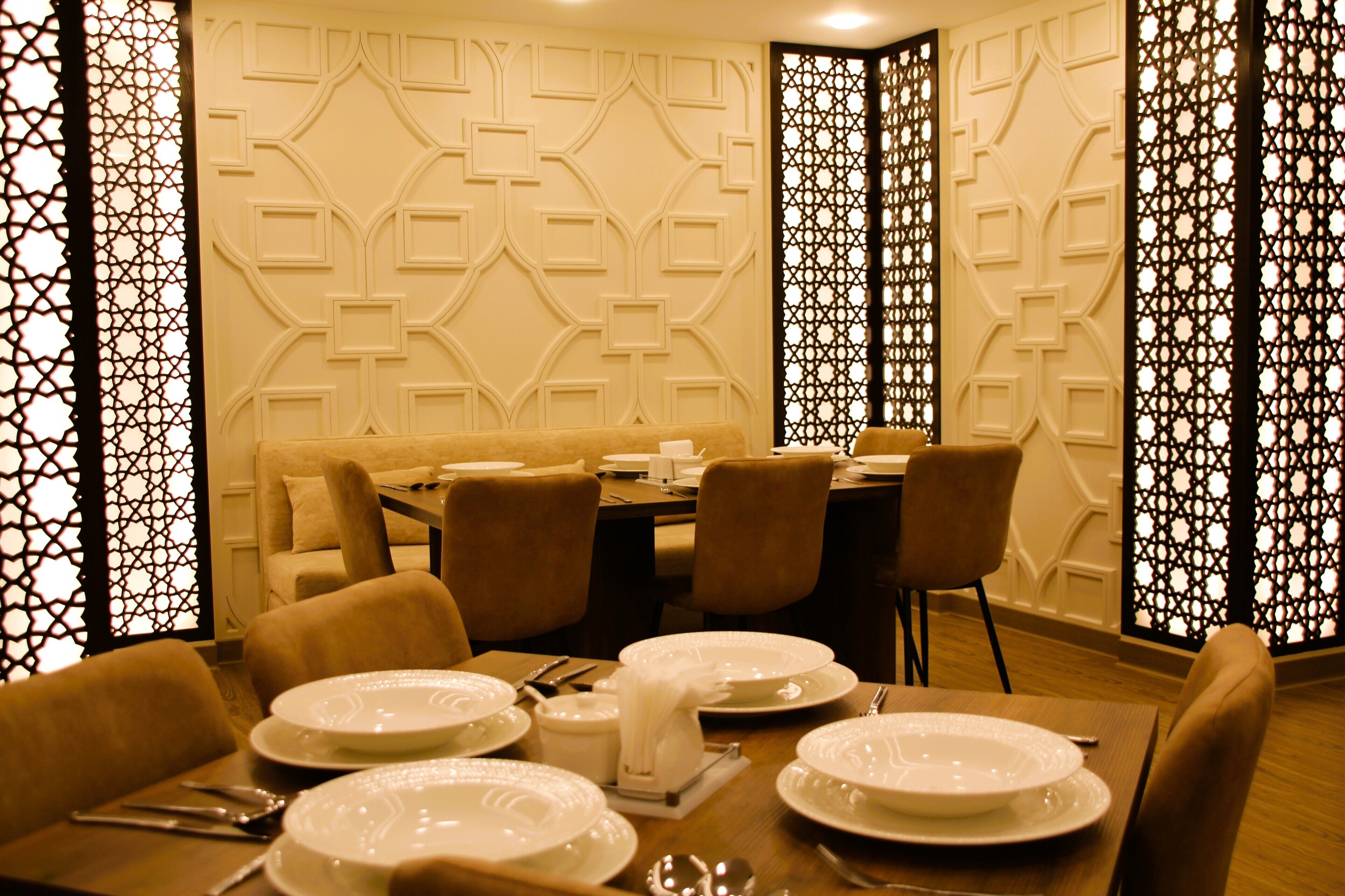 A dining area with a table set for four, surrounded by chairs, and a decorative wall with geometric patterns.