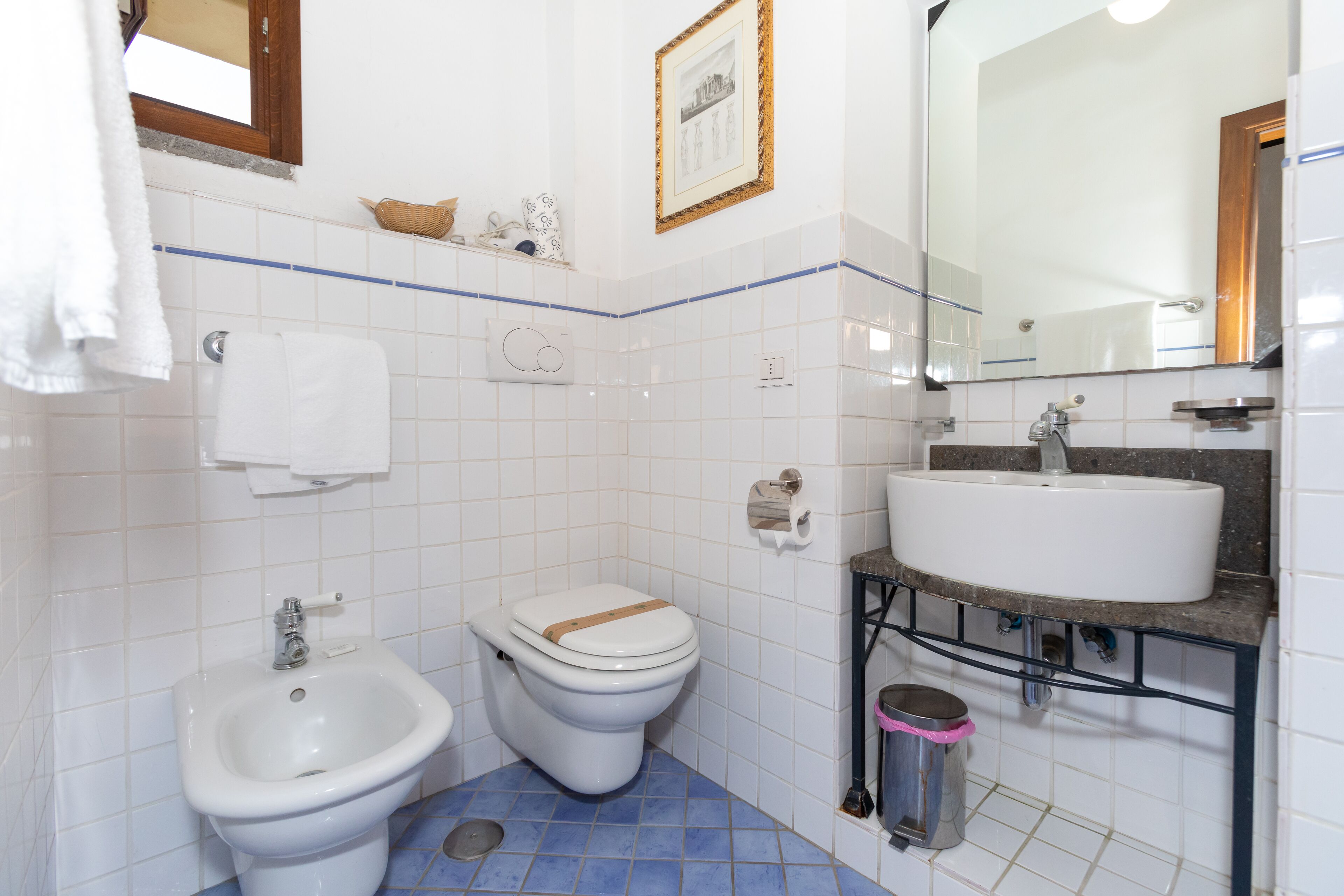 A bathroom with a bidet, toilet, sink, and a mirror.