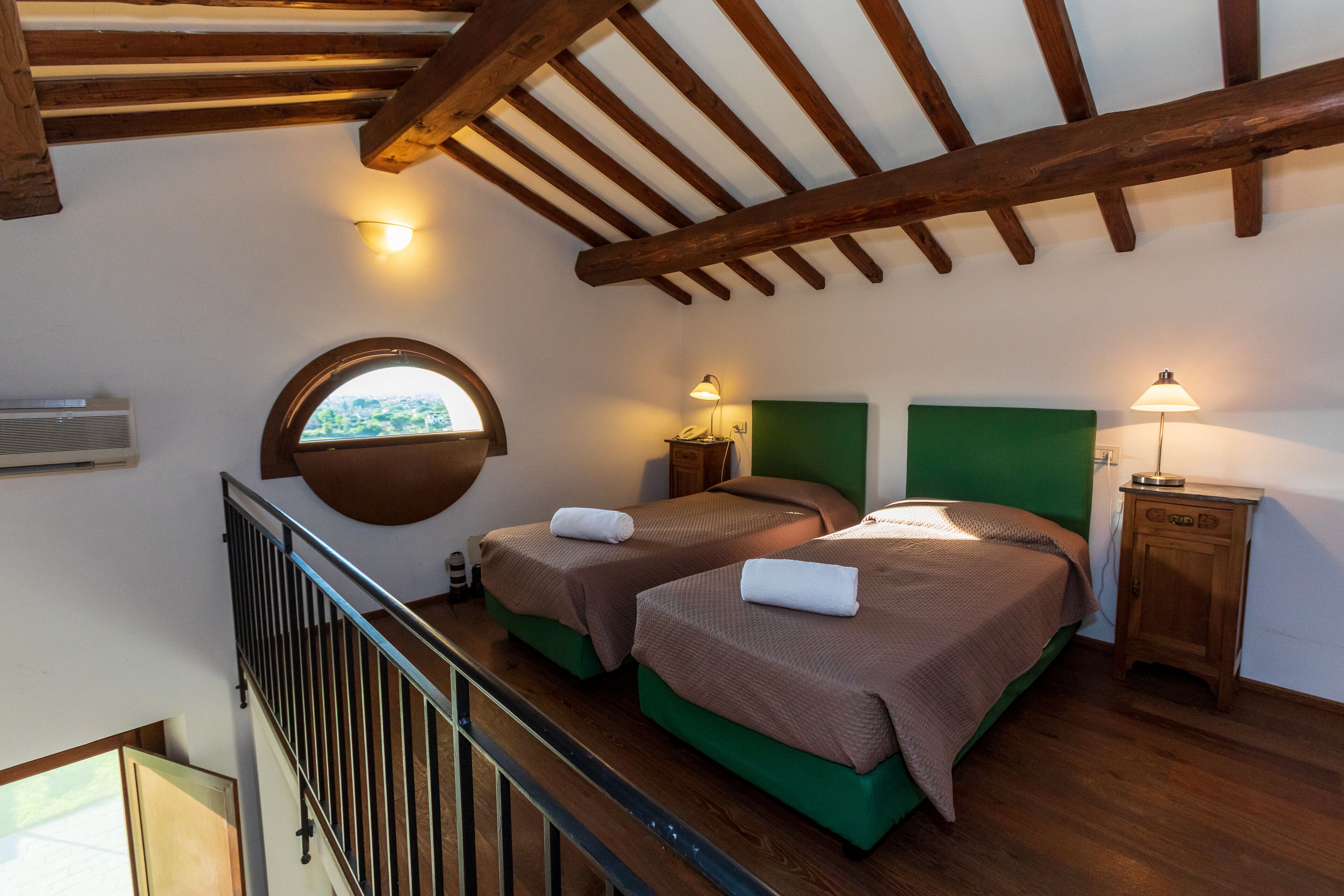 Ein Schlafzimmer mit zwei Betten, einem Fenster, einer Treppe und Holzbalken an der Decke.