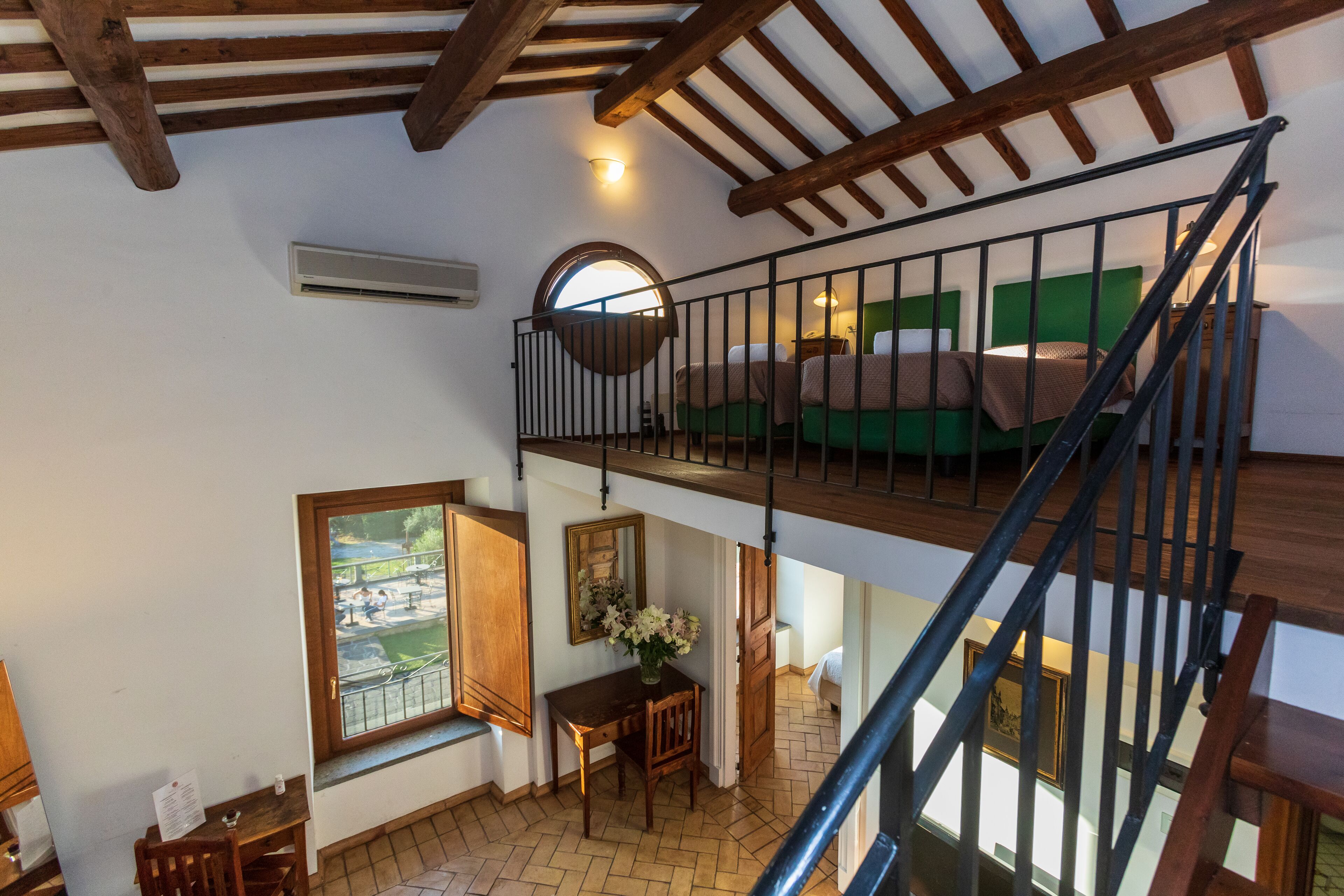 A multi-level room with a wooden staircase, a dining area with a table and chairs, and a bed with green bedding.
